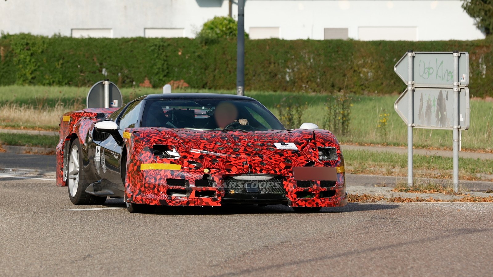 Camouflaged Ferrari 296 Challenge Stradale prototype in red-and-black wrap, front three-quarter view, testing on a road in Germany