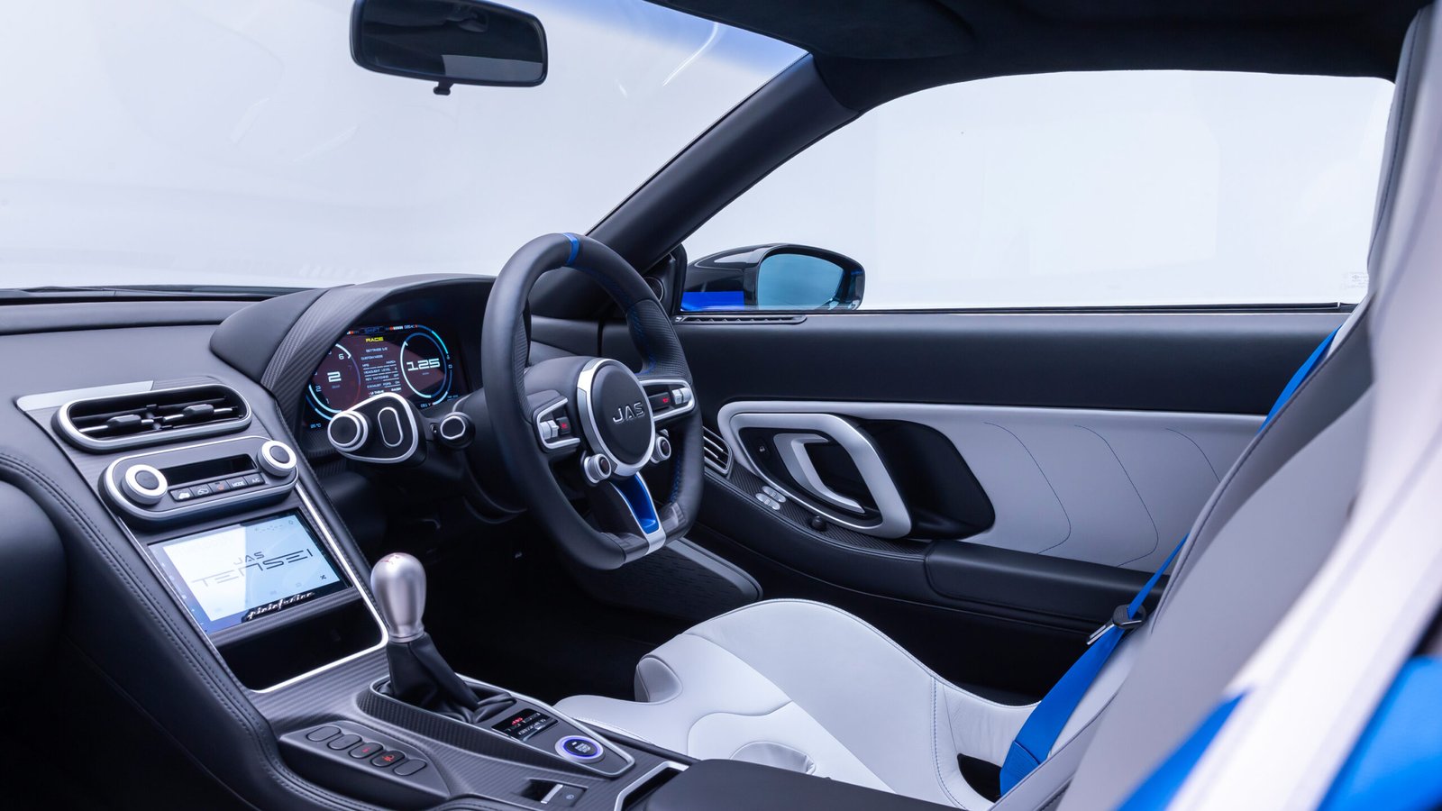 Interior of the JAS Tensei with a three-spoke steering wheel, digital gauges, a gated manual shifter and white and blue seats