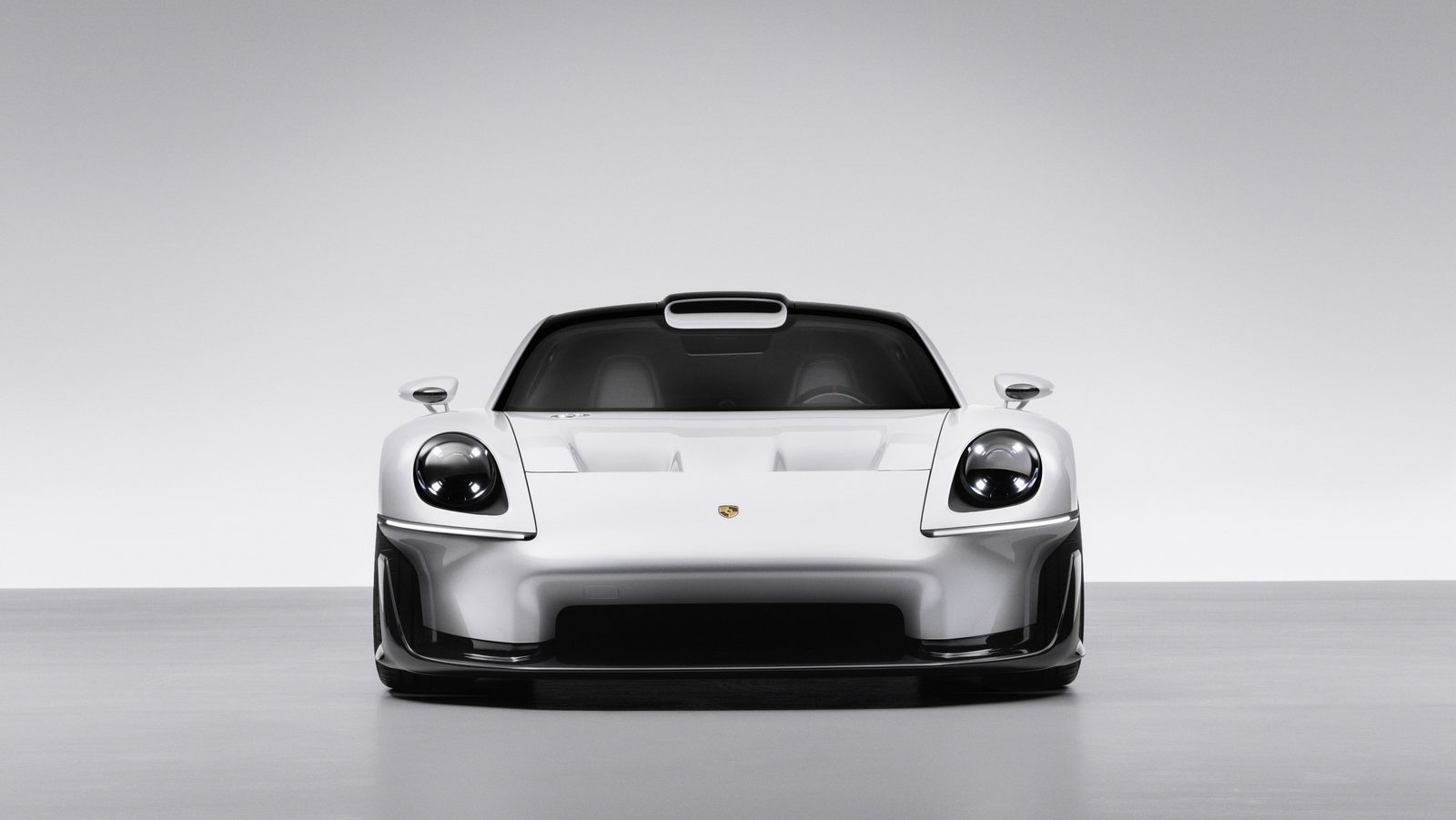 Head-on front view of the white Porsche Mission S showing two round headlights, a flat vented front hood with a Porsche crest, a dark lower intake and a slim roof scoop above the windshield
