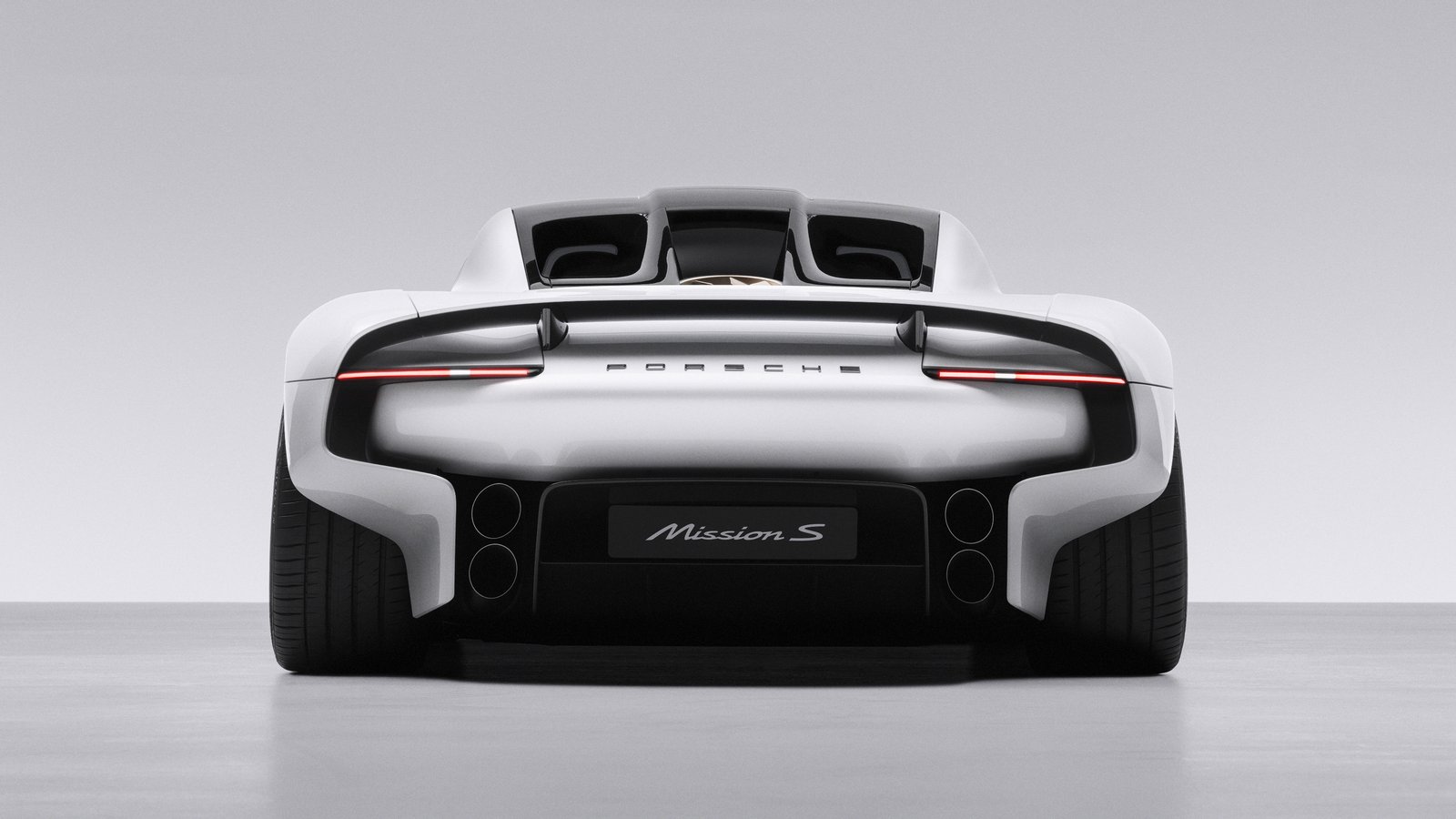 Rear view of the white Porsche Mission S vision model in a grey studio, showing the full-width light bar, Porsche lettering, a twin-intake rear deck with a cooling fan visible between them, quad exhaust outlets and a Mission S plate