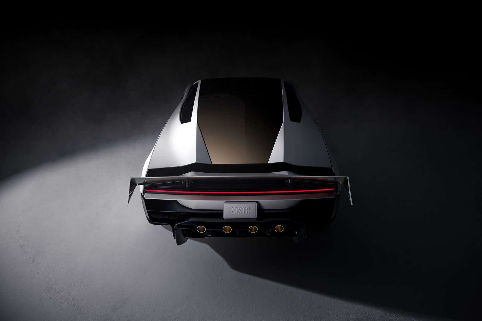 Overhead rear view of the white Tesla Roadster in a dark studio showing tinted glass, a wide rear wing, a thin red full-width taillight, an RDSTR license plate and four round gold-ringed ports low in the rear