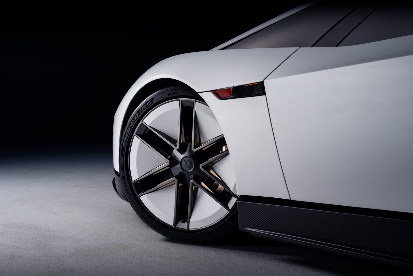 Close-up of the Tesla Roadster's front wheel: thin black spokes over a white wheel face, a Pirelli tire, a slim amber light strip ahead of the door and a carbon-fiber sill