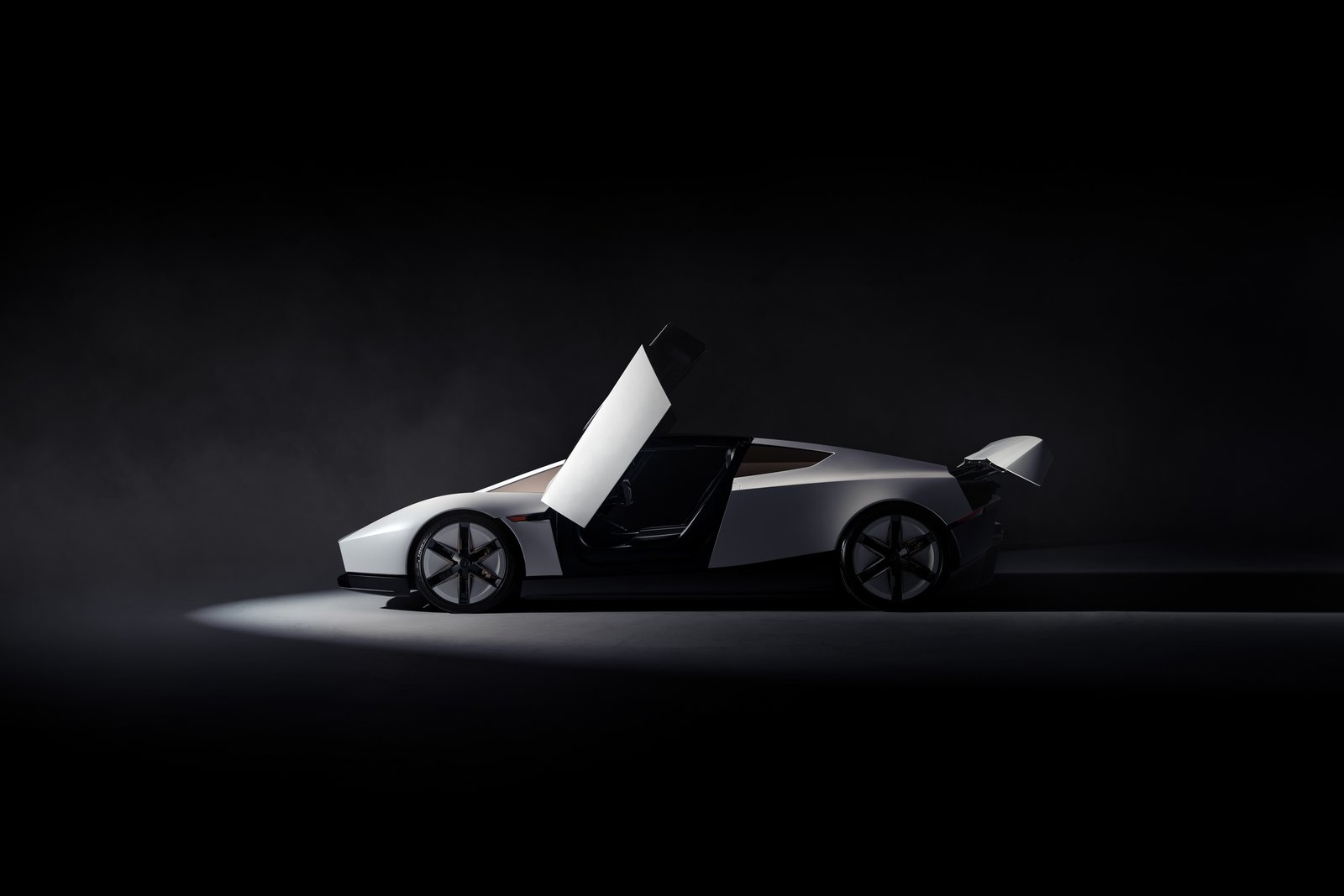 Side profile of the white Tesla Roadster in a dark studio, its upward-opening door raised, six-spoke black wheels and a raised rear wing
