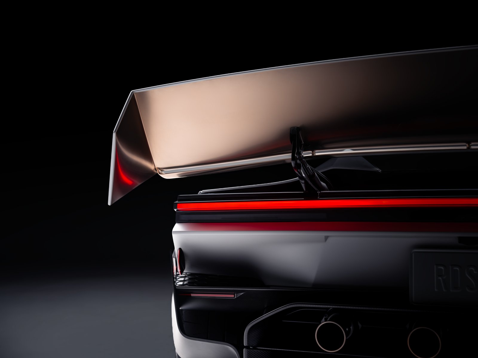 Close-up of the Tesla Roadster's raised rear wing above the full-width red taillight, with part of the RDSTR plate and two round rear ports visible